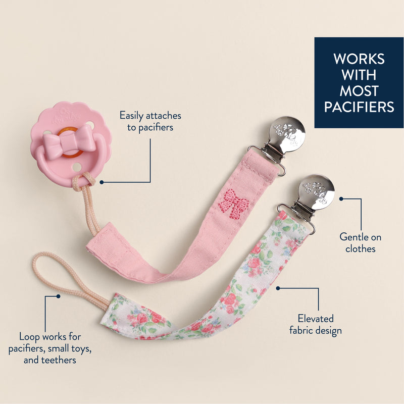 Pink pacifier clip with floral design on a beige background, featuring text describing its features.