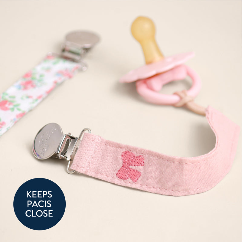 Pink pacifier clip with a bow design on a light background