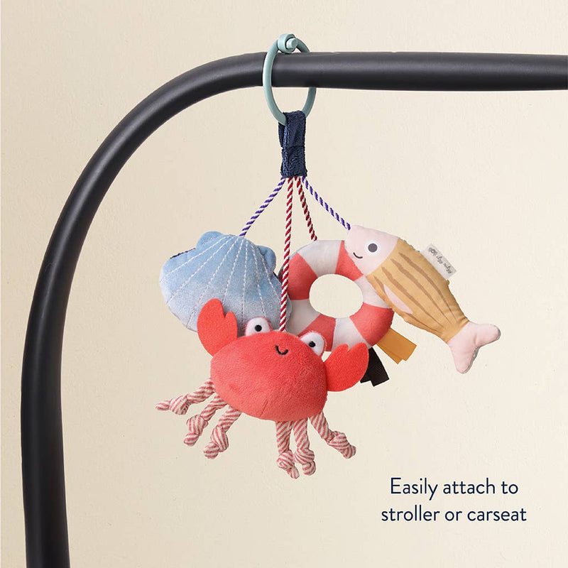 Set of colorful sea-themed plush toys hanging from a stroller bar on a beige background.