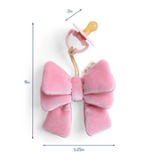 Pink velvet bow with a pacifier attached, shown with measurements on a white background