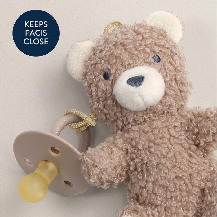 Teddy bear with a pacifier attached on a light background