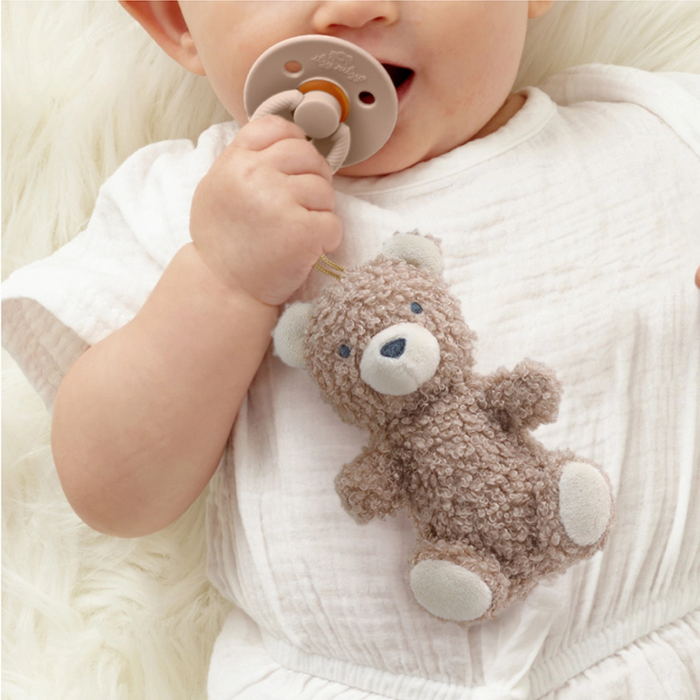 Baby holding a teddy bear toy and a pacifier on a soft surface