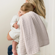 Woman holding a baby wrapped in a textured blanket.