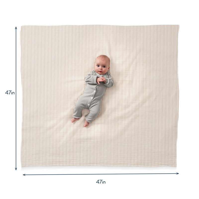 Baby in a gray onesie lying on a large striped mat with dimensions indicated.