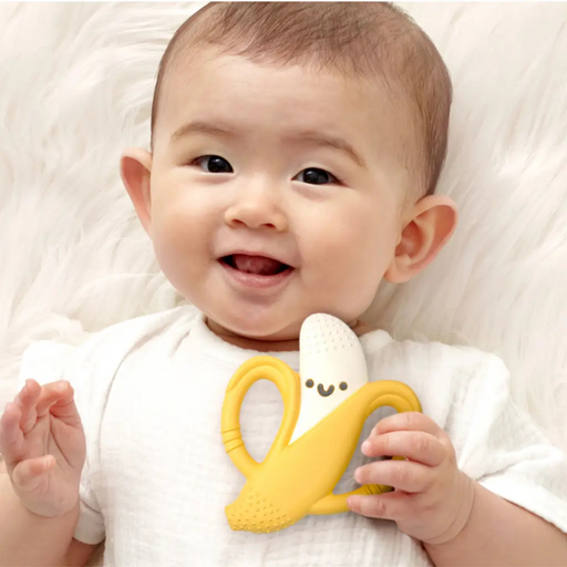 Baby holding a yellow teething toy with a smile on a white background