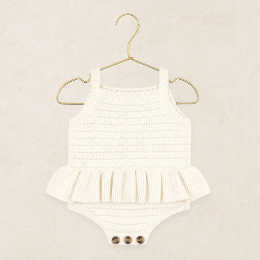 A white ribbed knit baby romper with a ruffled hem and three snap buttons at the crotch, displayed on a gold metal hanger against a textured beige background.