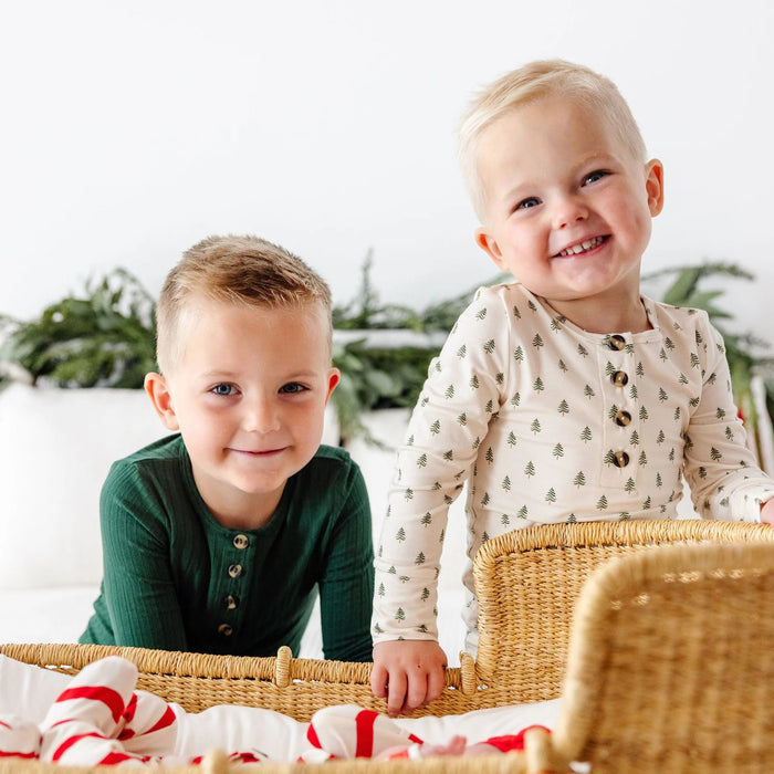 Two toddlers wearing Kevin Top and Bottoms in green and tree print sitting in a wicker basket