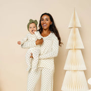 Woman and child in matching pajamas standing next to decorative paper trees on a beige background