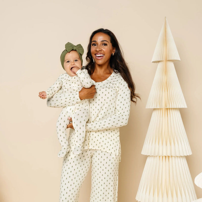 Woman and child in matching pajamas standing next to decorative paper trees on a beige background