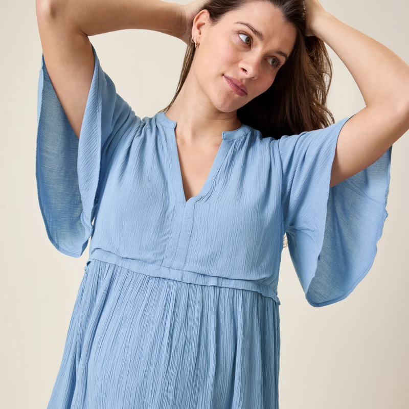Woman wearing a light blue dress with flowing sleeves against a neutral background