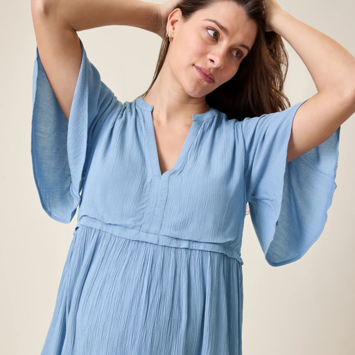 Woman wearing a light blue dress with flowing sleeves against a neutral background
