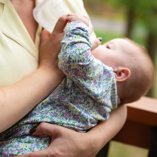 Baby in a floral outfit being held by an adult outdoors