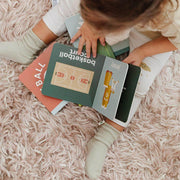 Child reading the Basketball Baby board book on a rug
