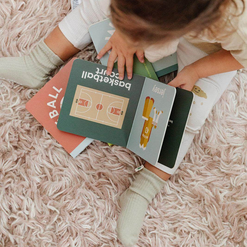 Child reading the Basketball Baby board book on a rug