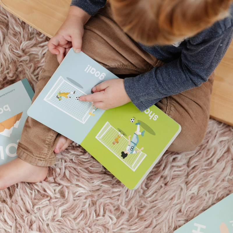 Toddler reading the Soccer Baby board book on a rug