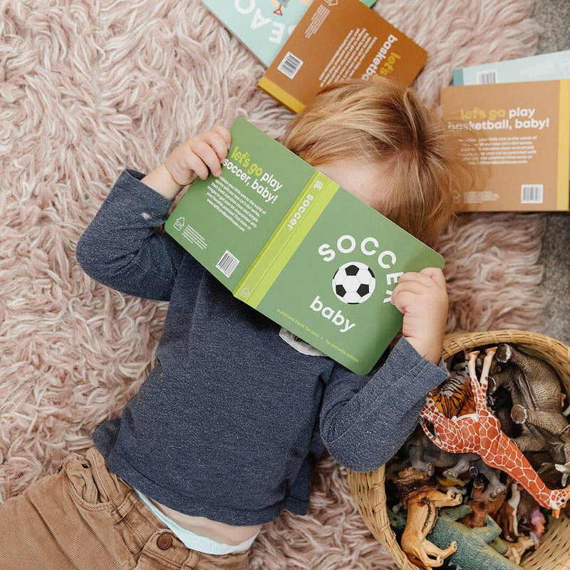 Toddler lying on a rug reading the Soccer Baby board book