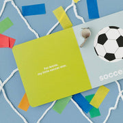 Soccer Baby board book open to the soccer ball page with confetti