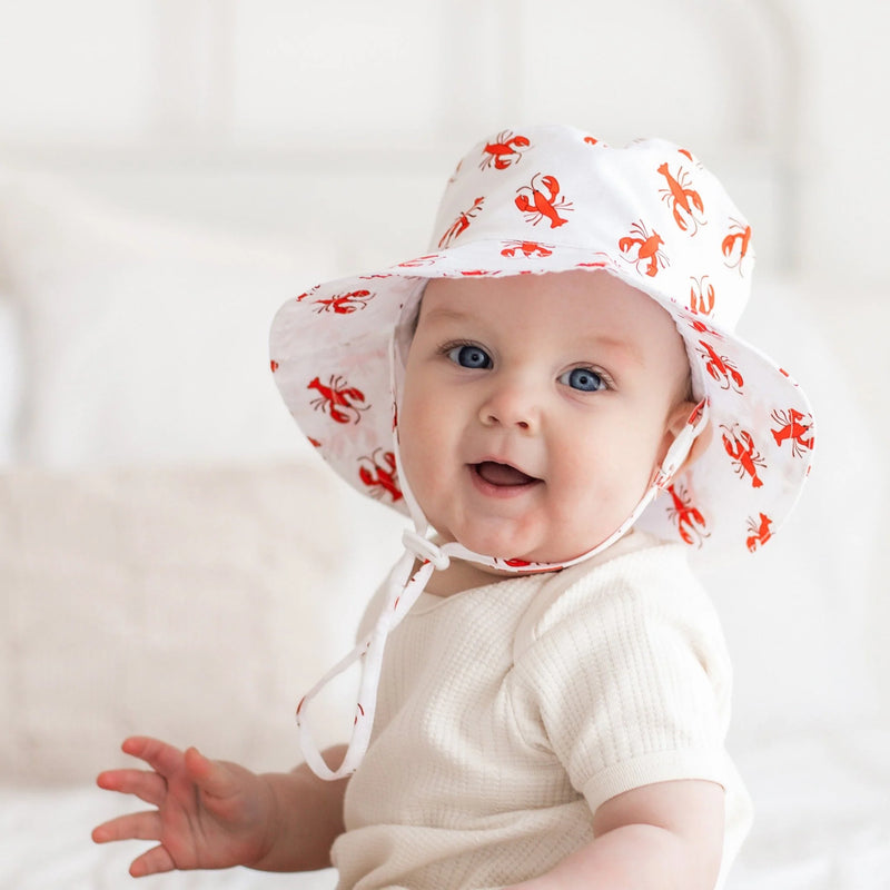 Baby wearing a white sun hat with red patterns on a light background