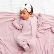 Baby in pink outfit with white headband lying on a pink blanket against a white background