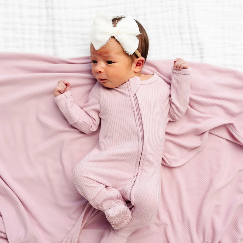 Baby in pink outfit with white headband lying on a pink blanket against a white background