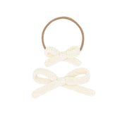 Two cream-colored bow hair ties on a white background