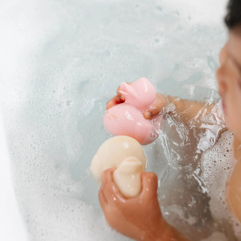 Child holding pink and cream Lou Lou & Co rubber duckies in a bubble bath