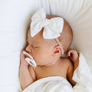 Newborn baby sleeping with a ivory Lou Lou & Co bow headband and pacifier