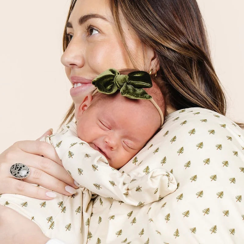Woman holding a baby wrapped in a blanket with green tree patterns, wearing a Lou Lou & Co olive headband