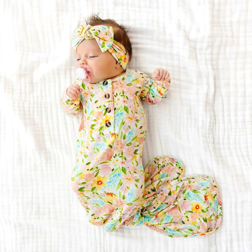 Newborn baby in a floral outfit and headband lying on a white textured surface