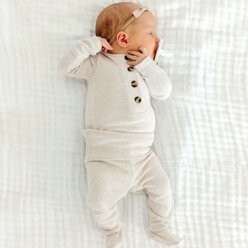 Newborn baby wearing a white onesie with buttons on a white textured blanket