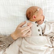 Newborn baby in a beige outfit with a headband, held by an adult hand on a white background