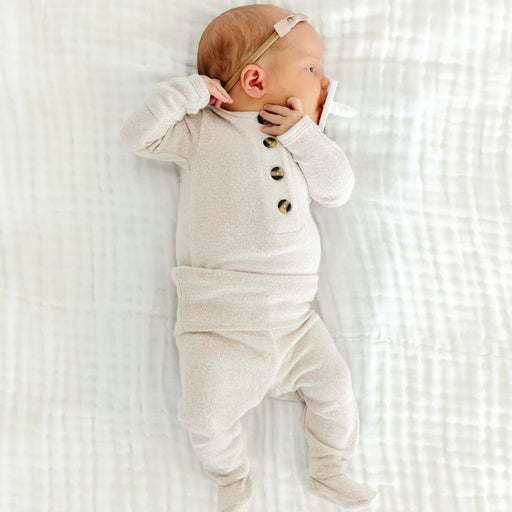 Newborn baby wearing a white onesie with buttons on a white textured blanket