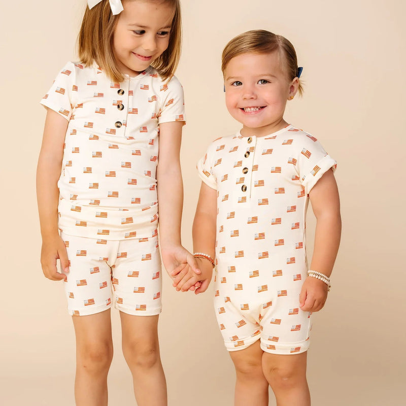 Two children wearing matching pajama sets with car pattern on a beige background