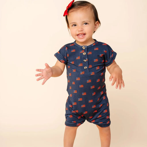 Baby wearing a navy blue romper with red patterns on a beige background