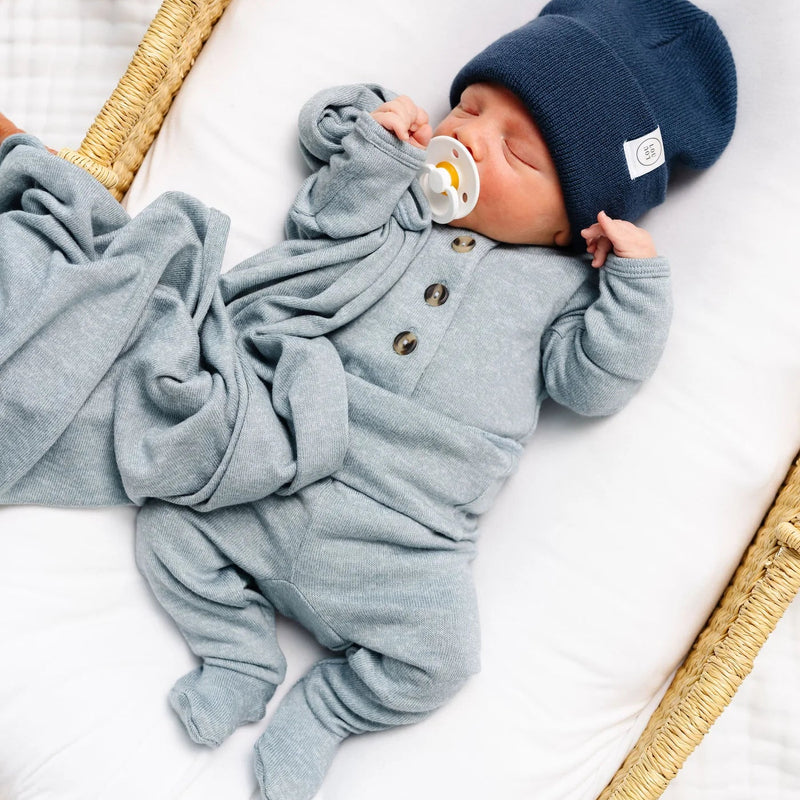 Newborn baby in a blue outfit and hat lying in a basket.