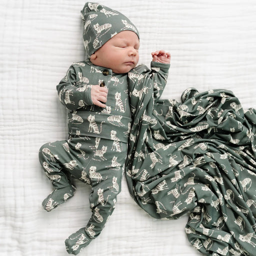 Newborn baby in green animal print onesie and hat, wrapped in matching blanket on white background