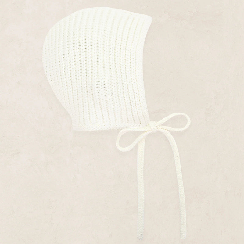 White knitted bonnet with a bow on a beige background