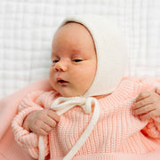 Newborn baby in a pink knitted outfit with a white hood on a light background