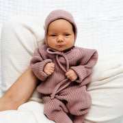 Baby in a pink knitted outfit being held on a white background