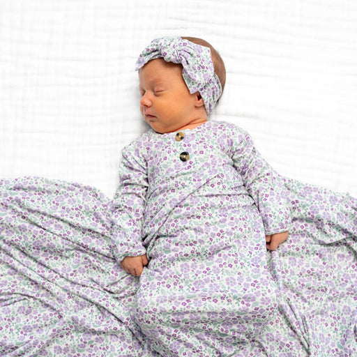 Newborn baby in a floral outfit and headband lying on a white blanket