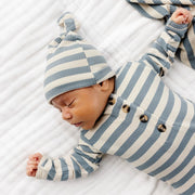 Baby wearing a blue and white striped outfit and hat, sleeping on a white surface.