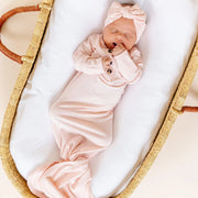 Newborn baby in a pink outfit and headband sleeping in a Moses basket.
