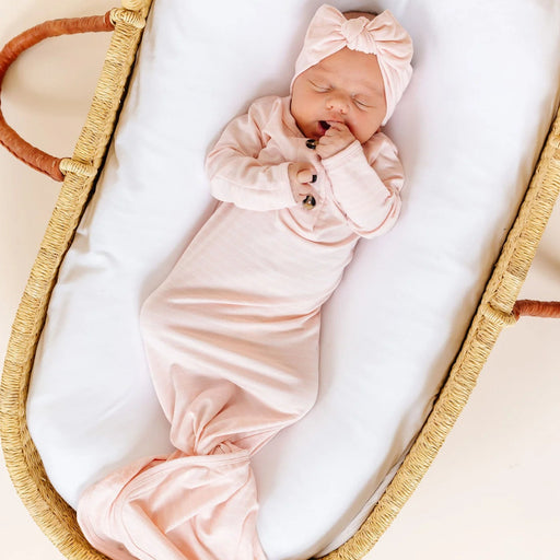 Newborn baby in a pink outfit and headband sleeping in a Moses basket.