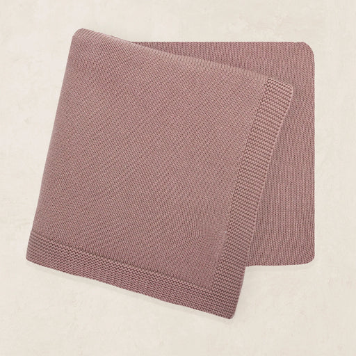 Folded pink knitted blanket on a beige background