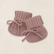 Pair of pink knitted baby booties on a beige background