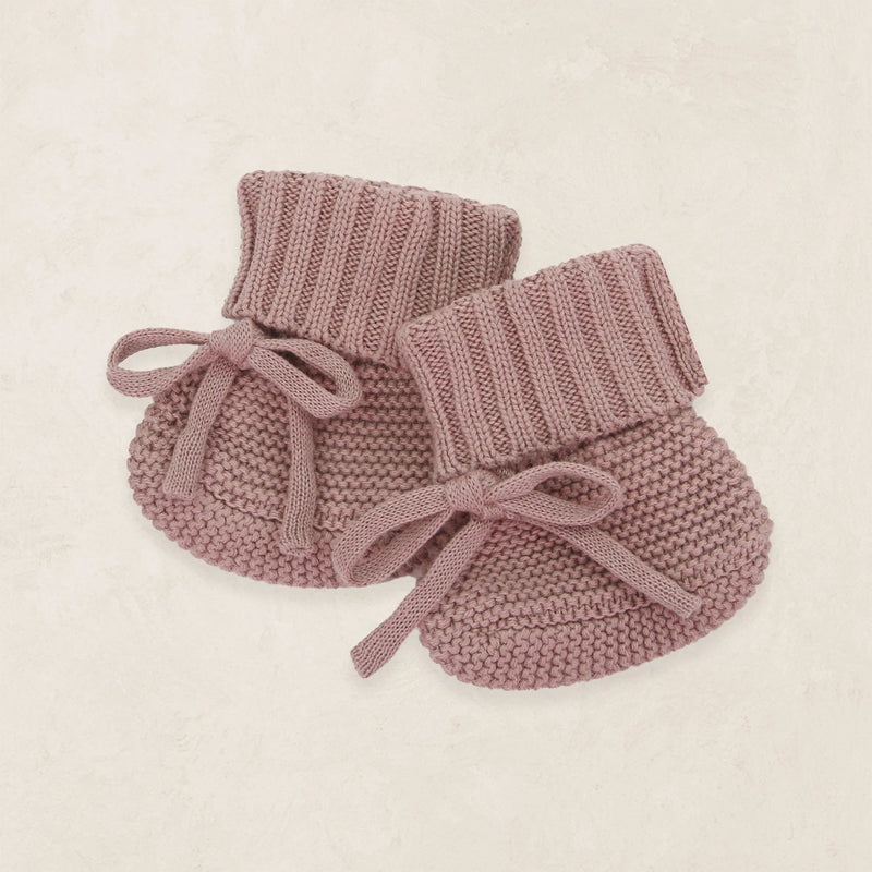 Pair of pink knitted baby booties on a beige background