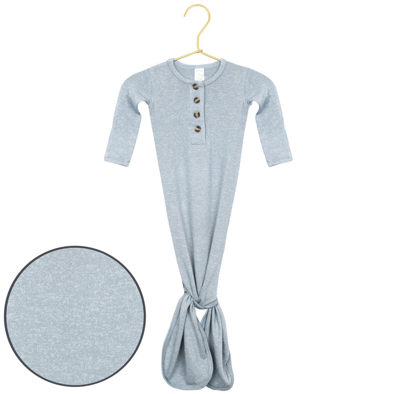 A light heather gray long-sleeve baby tunic with a buttoned henley neckline and a gathered tie at the bottom, shown hanging on a gold hanger with a circular fabric detail inset on the bottom left.