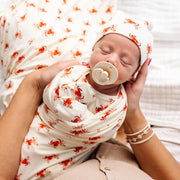 Newborn baby wrapped in a patterned blanket with a pacifier, held by an adult.