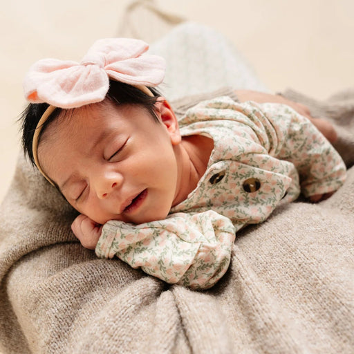 Newborn baby sleeping peacefully with a pink bow headband and floral outfit.