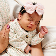 Newborn baby wearing a floral outfit and pink headband, lying on a white surface.